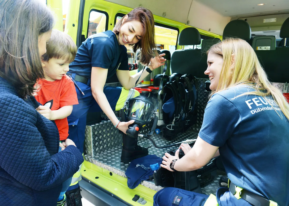 Zwei Frauen zeigen einem kleinen Jungen die Ausrüstung der Feuerwehr. 